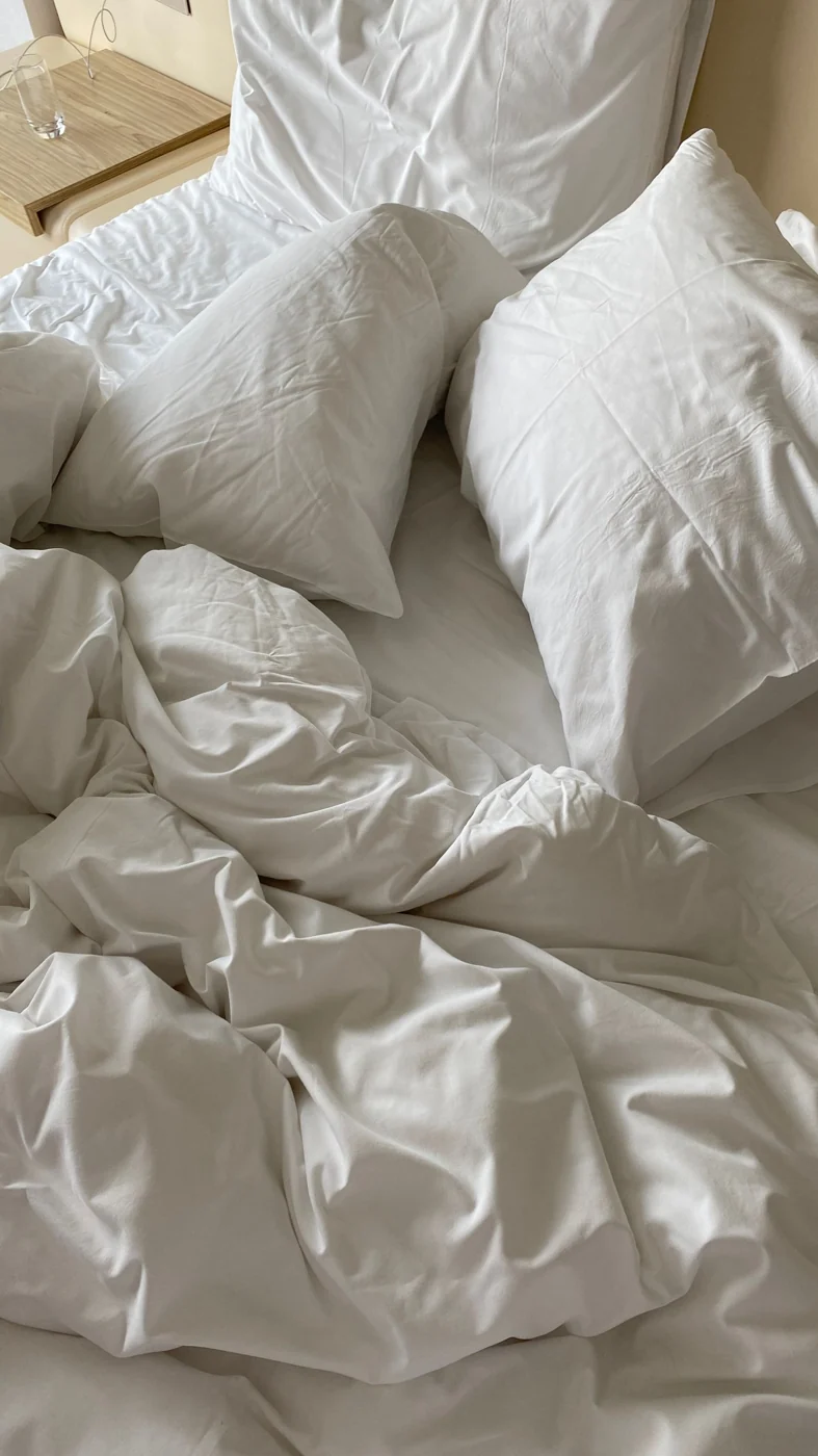 Top view of a cozy, inviting bed with white linen and pillows in a minimalist bedroom setting.
