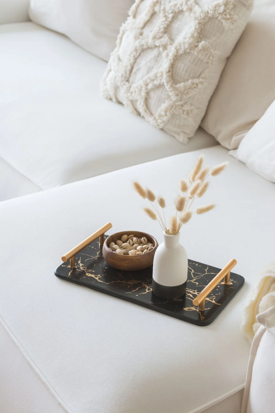 A cozy white sofa with a black marble tray featuring a vase and nuts, perfect for modern home decor.