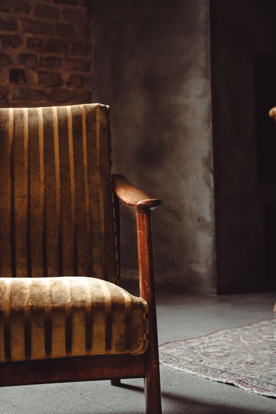 A beautifully lit vintage wooden armchair with a striped cushion in a warm, cozy indoor setting.