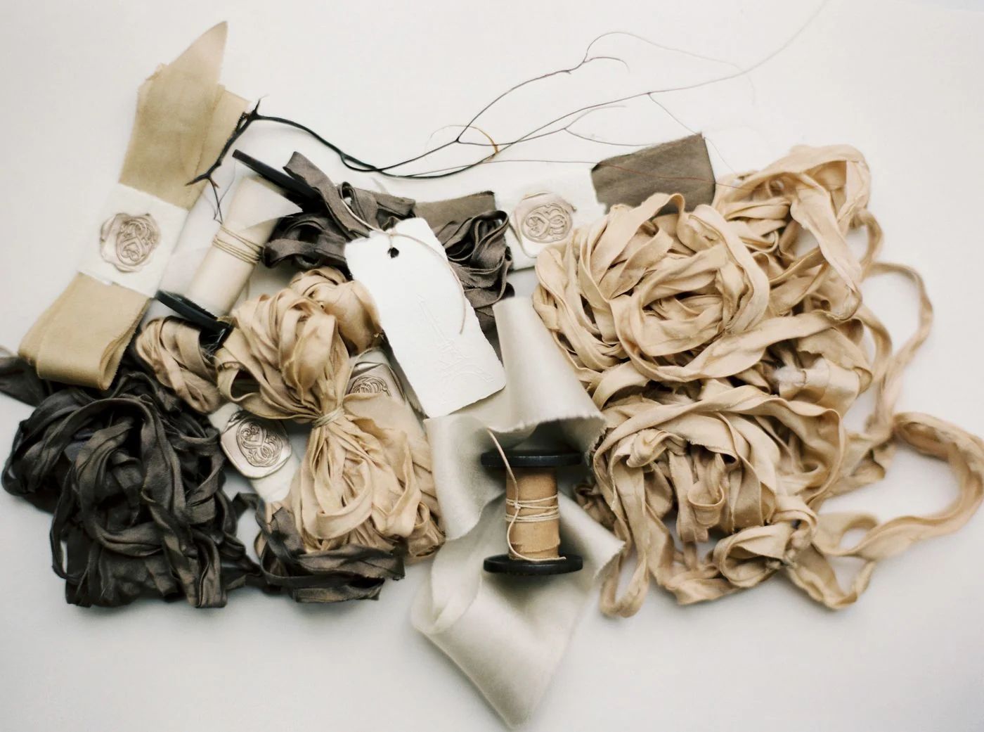 A top view of assorted ribbons, strings, and fabric for crafting on a white surface.