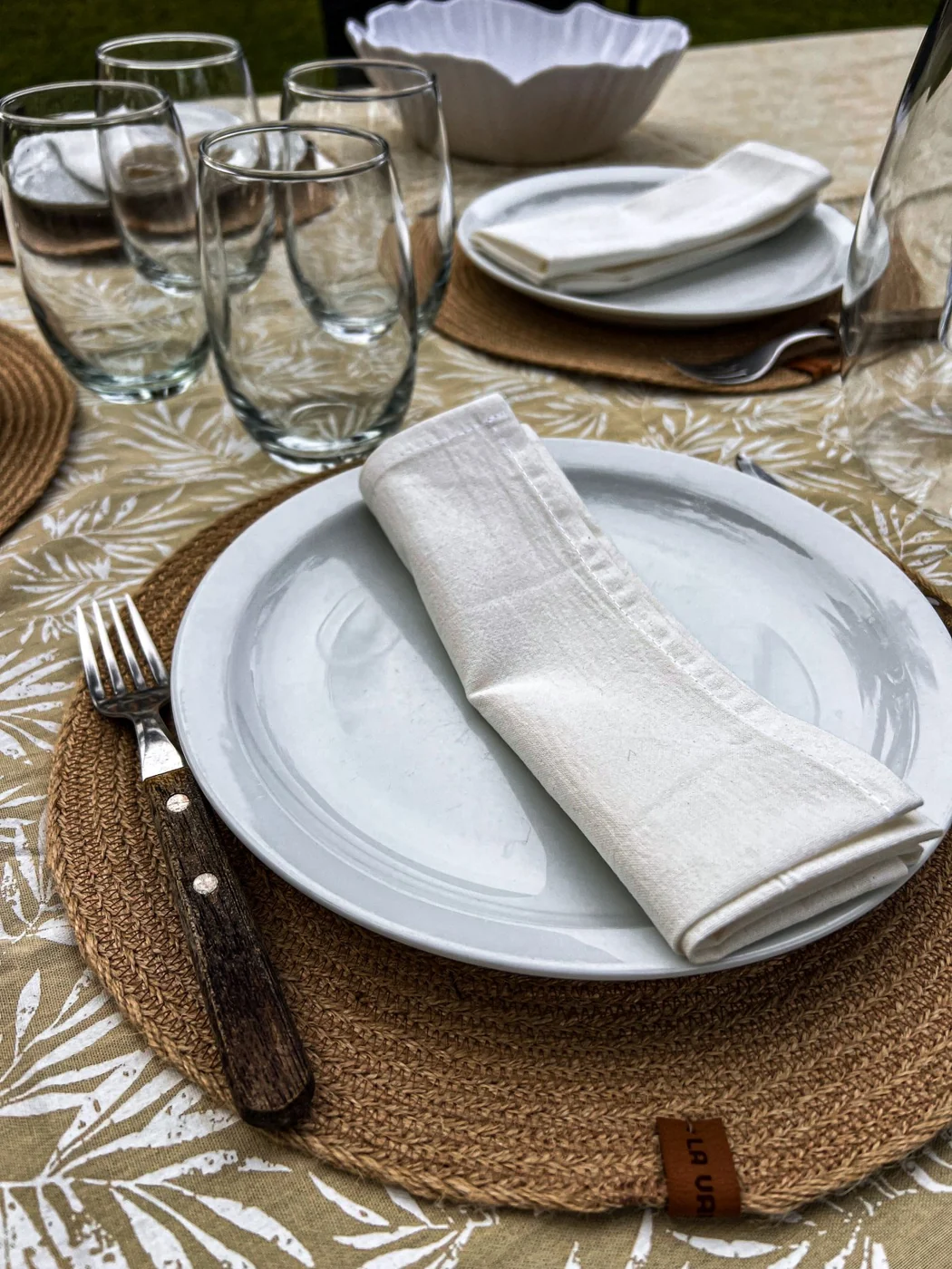 An elegantly arranged table setting featuring white plates, napkins, cutlery, and glasses on a patterned tablecloth.