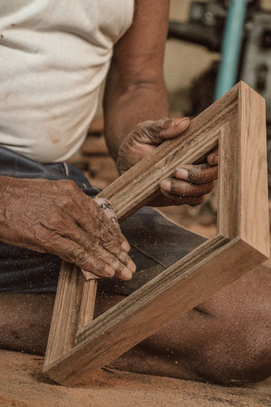 Close-up of a senior man sanding a wooden frame, showcasing traditional craftsmanship and skill.