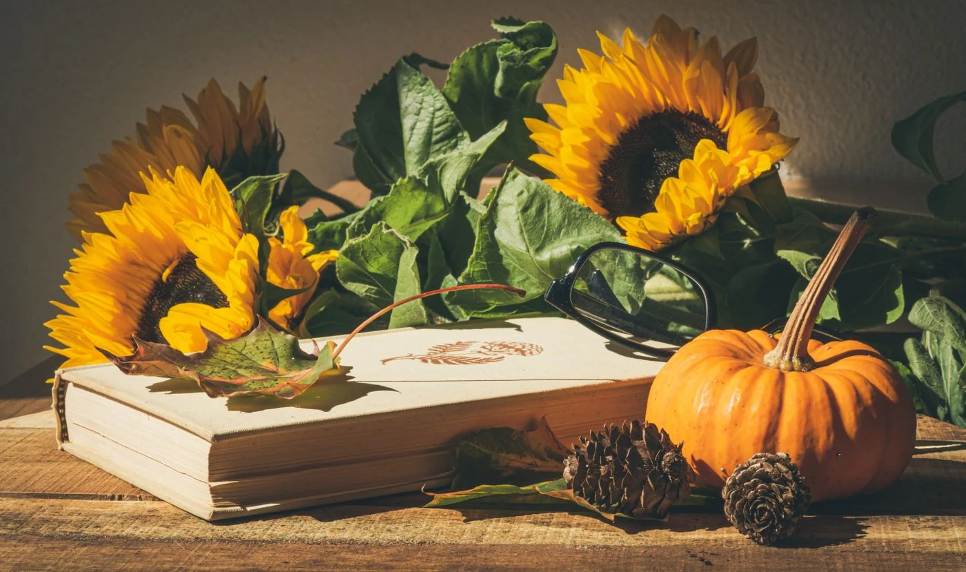 Cozy autumn still life featuring sunflowers, a pumpkin, and a book on a wooden table.