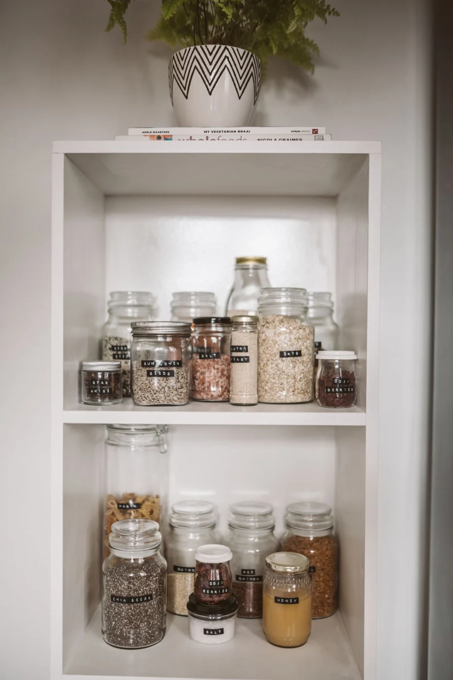 Neatly arranged pantry showcasing labeled glass jars with assorted grains and seeds.