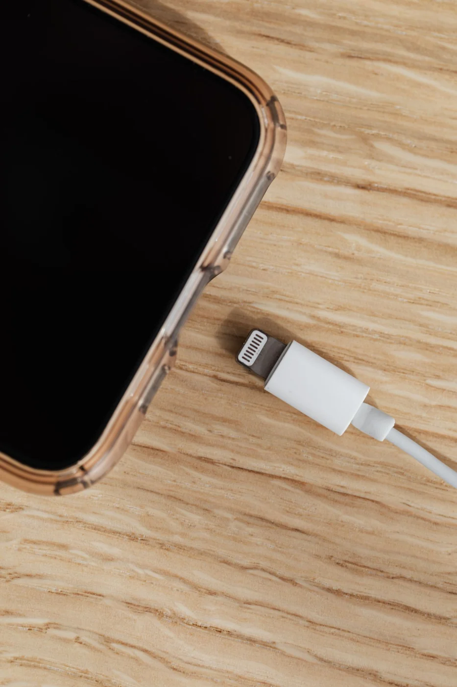 Close-up of a smartphone charging cable next to a phone on a wooden desk.