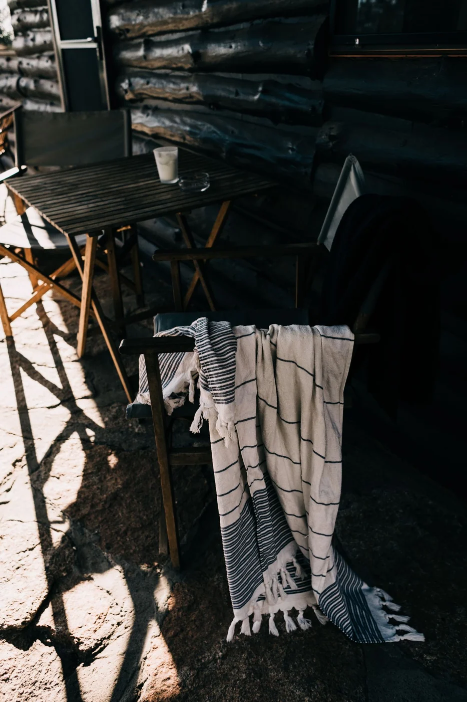 A sunlit rustic outdoor terrace with cozy blankets and wooden furniture, perfect for relaxation.