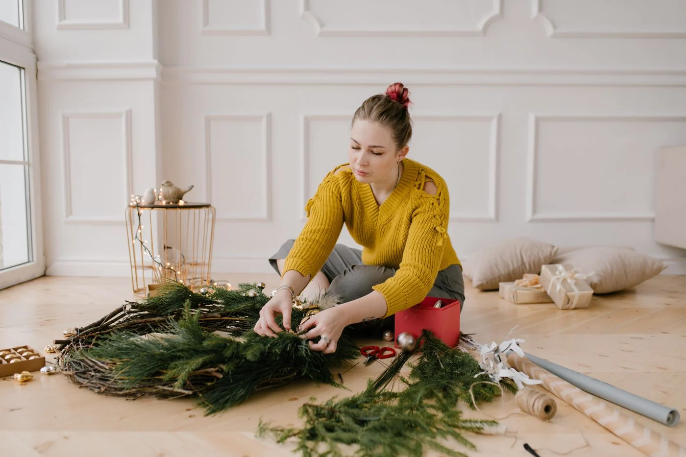 Woman decorating a Christmas wreath inside a cozy room, focused on holiday preparations.