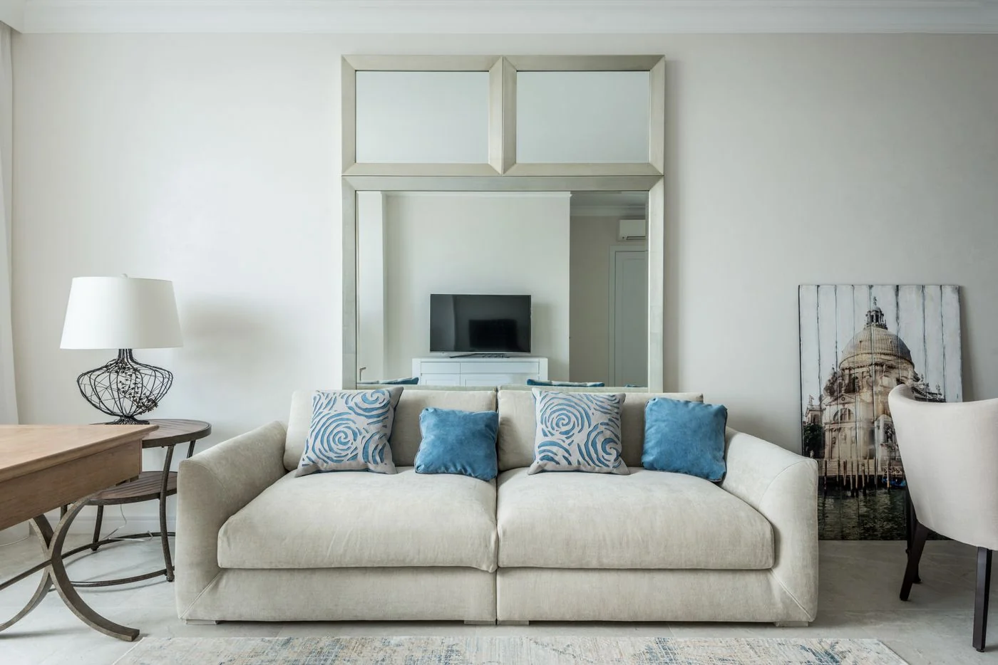 A pale sofa with blue cushions and a mirror in a light living room.