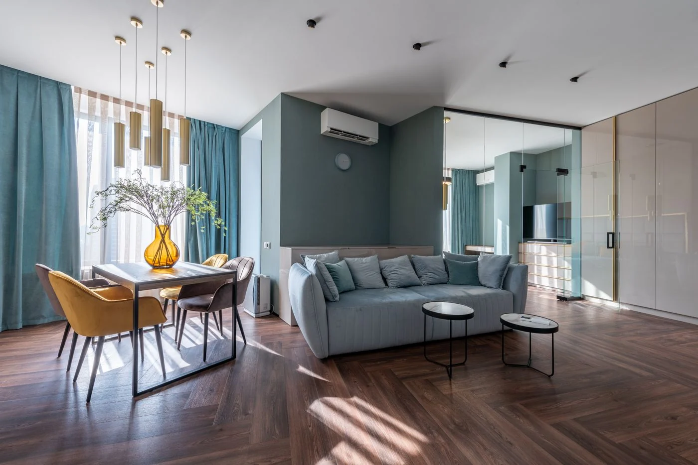 A blue-gray sofa and dining chairs in a room with pale curtains and a wooden floor.