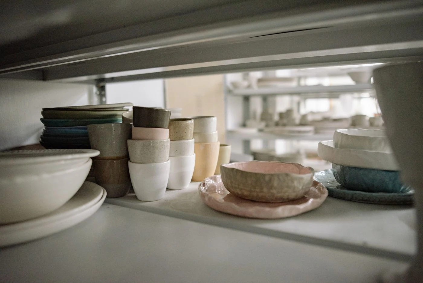 A collection of elegant ceramic dishes and cups organized on storage shelves.