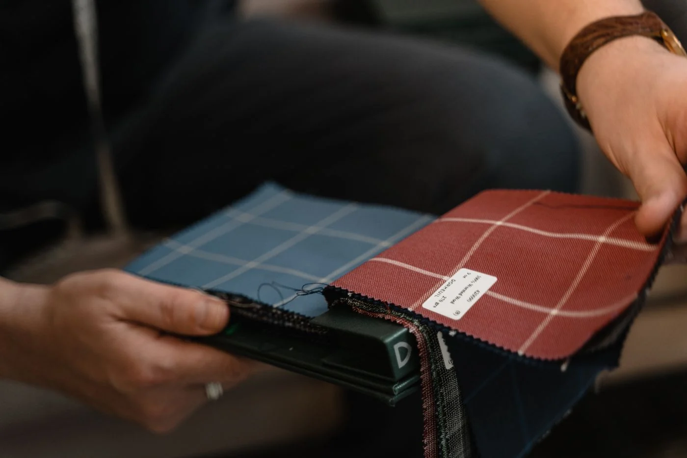 Close-up of hands holding fabric swatches with plaid patterns, ideal for design and textile projects.