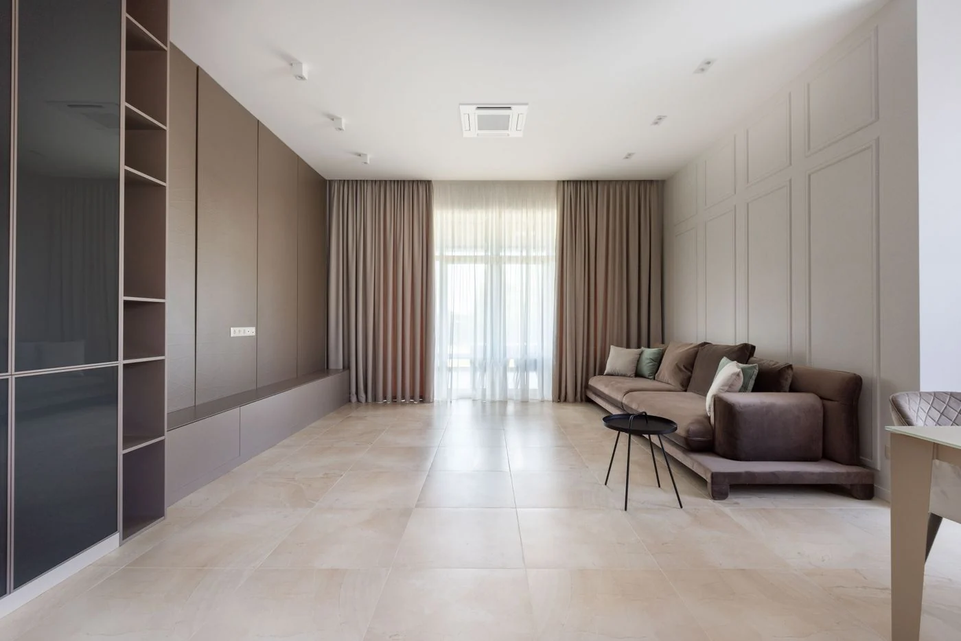 Spacious modern living room interior with a sofa, shelves, and curtains.