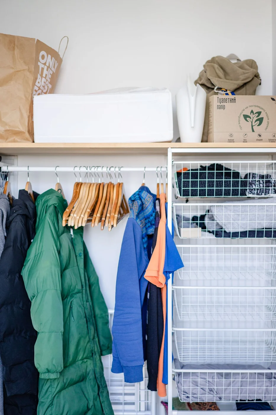 Neatly arranged clothes on hangers in a closet with wire storage baskets offering home organization.